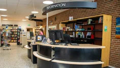Informationsdisken på stadsbiblioteket i Strömstad är välvd och rundad i svart och ljust trä. På disken står skärmar och skyltar. Väggen bakom är i rött tegel liksom utsidan på huset.