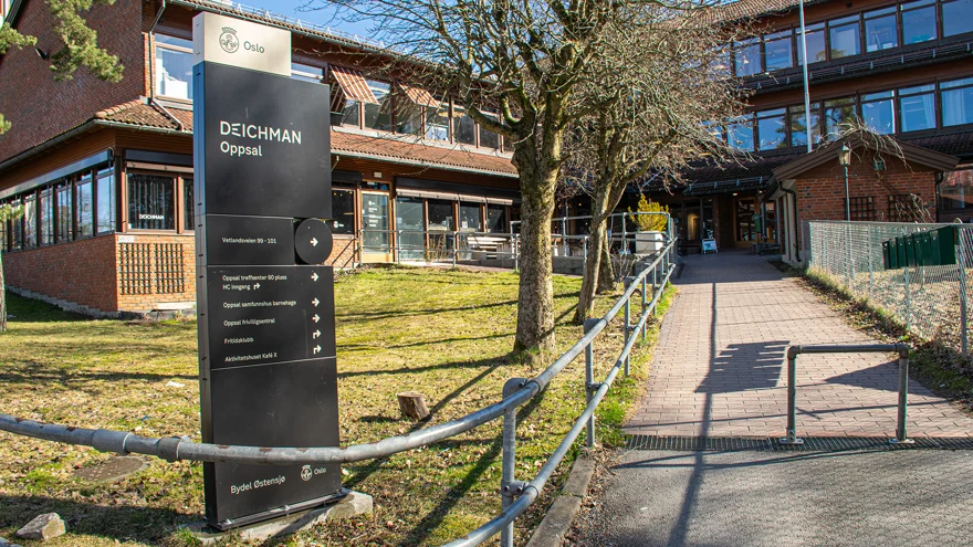 Exteriör av biblioteket och byggnaden det ligger i. En gångväg går upp till byggnaden som är i två våningar och byggd i rött tegel. Den sitter ihop med en annan trevåningsbyggnad i samma stil. Solen skiner och det är vår ute.