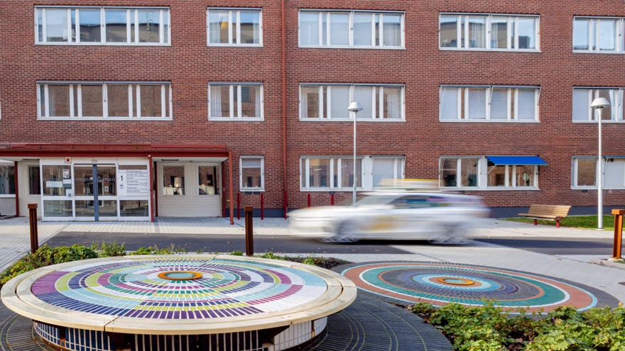 Rundlar med färgade kakelplattor. I bakgrunden en röd tegelbyggnad och en taxibil.