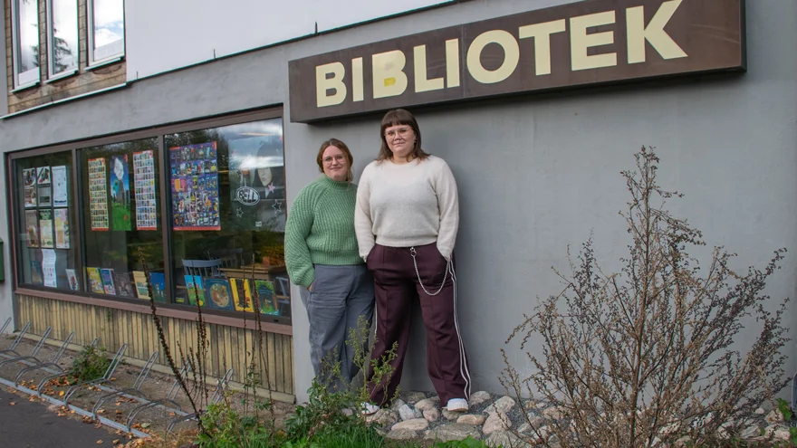 Mia-Marika Andin, bibliotekarie Horreds bibliotek och Louise Öjborg, bibliotekarie Fritsla bibliotek står utanför biblioteket i Horred. De står under en skylt där det står BIBLIOTEK.
