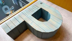 En stor träskulptur i formen som ett stort P. Den ligger plant mot golvet och på den står ord skrivna som innehåller bokstaven P.