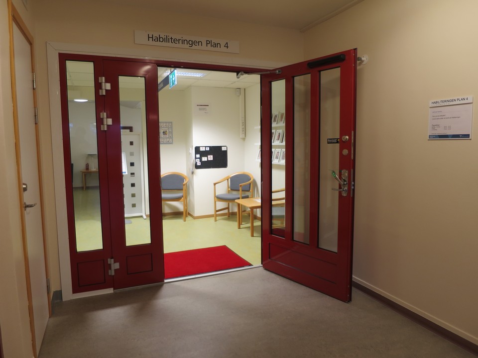 Entrédörr i glas med röda detaljer i korridor